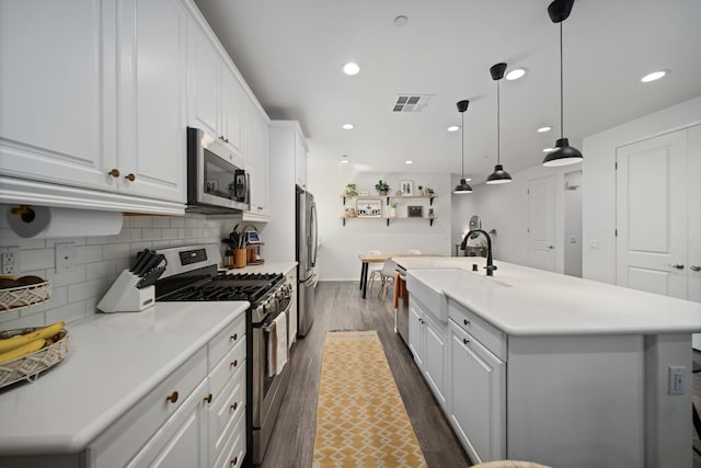 kitchen featuring tasteful backsplash, visible vents, white cabinets, a kitchen island with sink, and stainless steel appliances