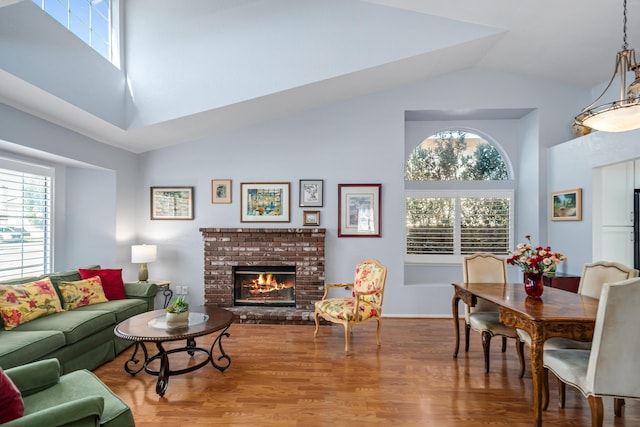 living room with hardwood / wood-style floors, a healthy amount of sunlight, high vaulted ceiling, and a brick fireplace