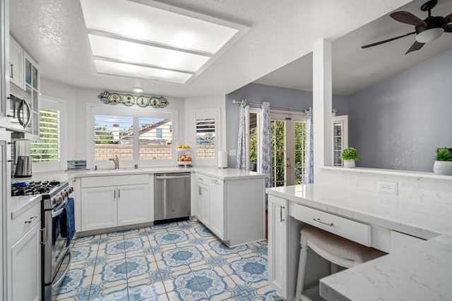 kitchen featuring sink, stainless steel appliances, light stone counters, kitchen peninsula, and white cabinets