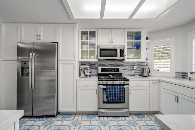 kitchen with light stone countertops, backsplash, stainless steel appliances, sink, and white cabinetry