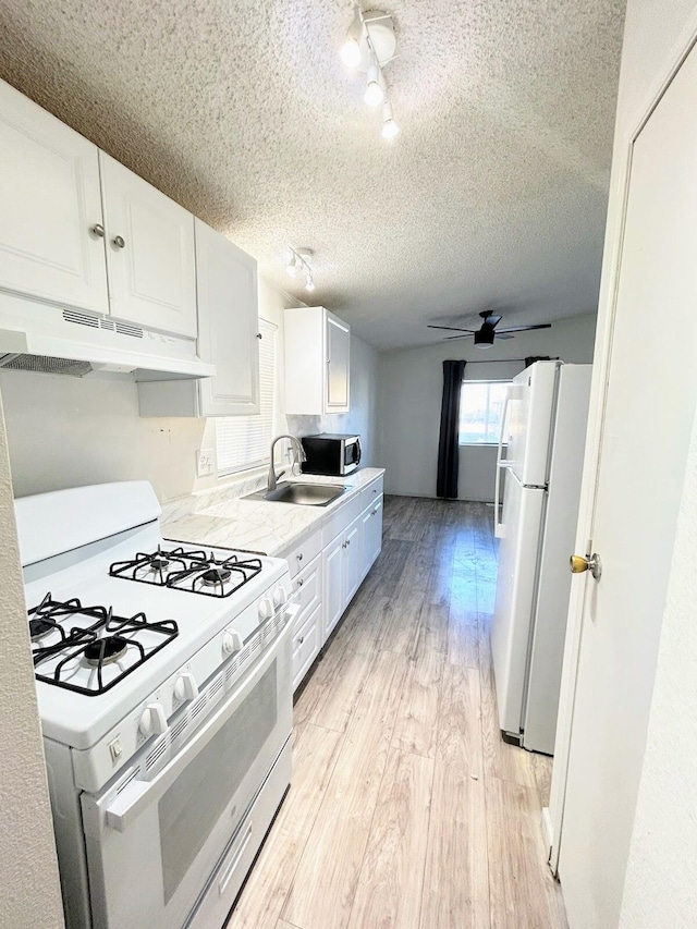 kitchen featuring light wood-type flooring, a textured ceiling, white appliances, sink, and white cabinetry