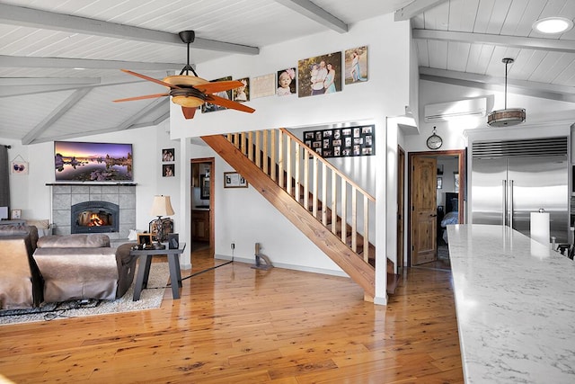 living room with wood-type flooring, lofted ceiling with beams, wooden ceiling, a tile fireplace, and ceiling fan