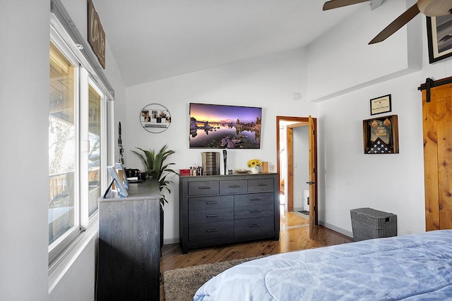 bedroom with dark hardwood / wood-style floors, vaulted ceiling, a barn door, and ceiling fan