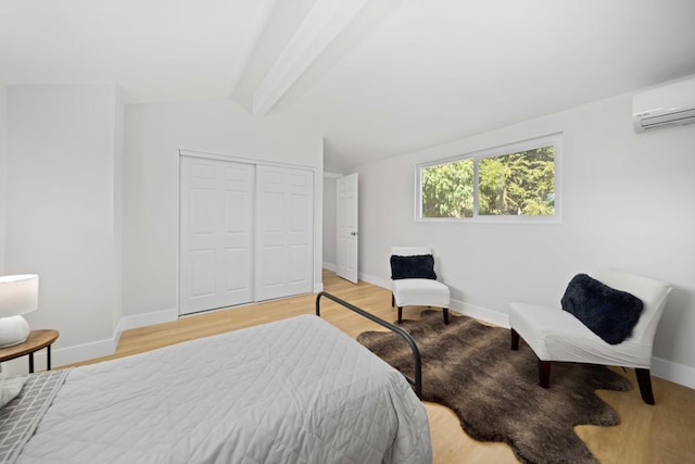 bedroom featuring a wall mounted AC, vaulted ceiling with beams, light hardwood / wood-style flooring, and a closet