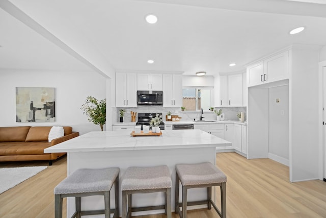 kitchen featuring light stone countertops, light wood-type flooring, stainless steel appliances, a kitchen island, and white cabinetry