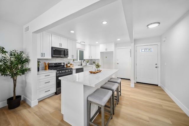 kitchen featuring a breakfast bar, white cabinets, light stone countertops, a kitchen island, and stainless steel appliances