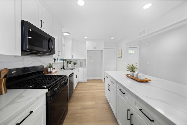 kitchen featuring light stone countertops, light wood-type flooring, sink, black appliances, and white cabinets