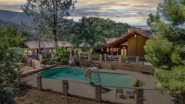 pool at dusk featuring a diving board, fence, a mountain view, and a fenced in pool