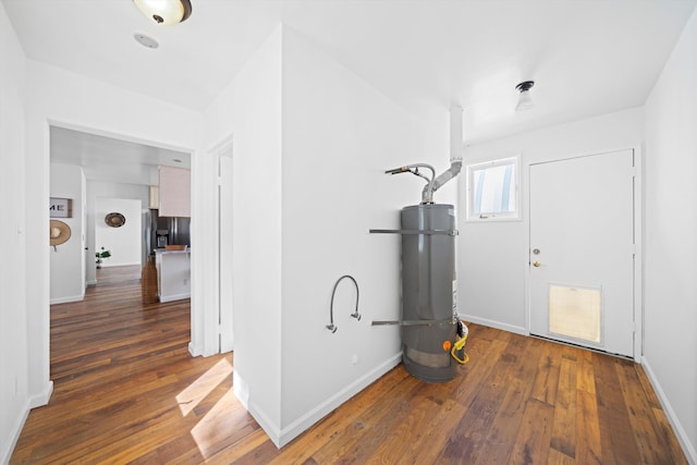 hall with secured water heater, wood-type flooring, and baseboards