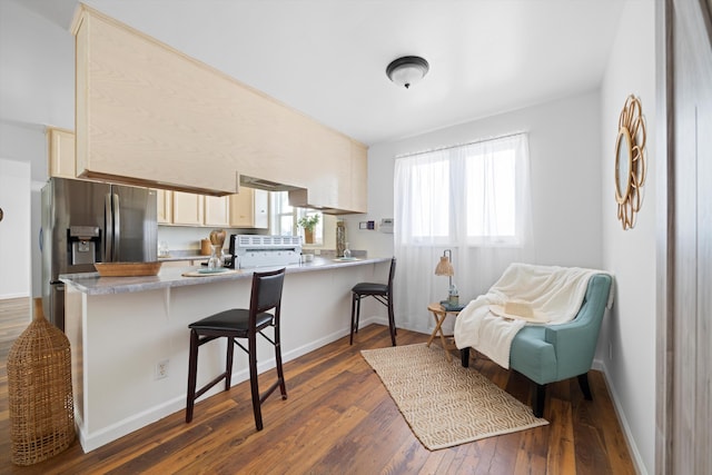 kitchen with stainless steel fridge, a kitchen breakfast bar, dark wood finished floors, a peninsula, and light countertops
