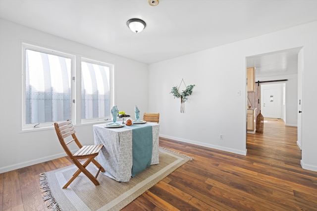 dining area featuring dark wood finished floors, baseboards, and a barn door