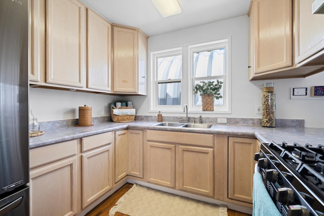 kitchen featuring a sink, stove, light brown cabinetry, stainless steel fridge, and light wood finished floors