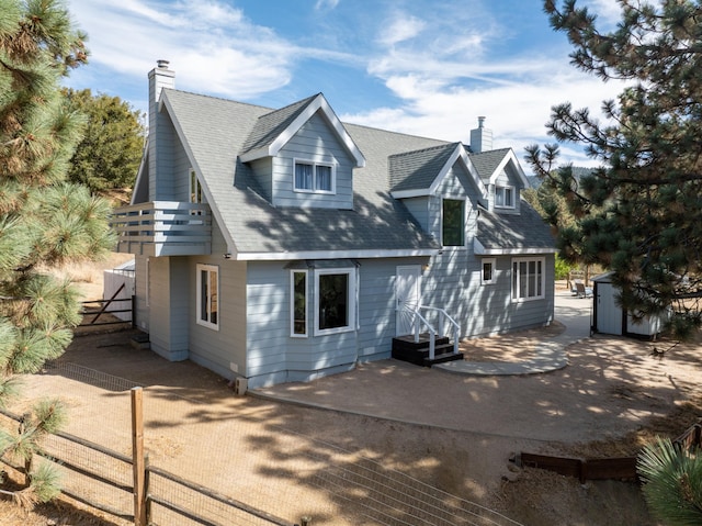 back of house with a storage shed, a chimney, an outdoor structure, fence, and a patio area
