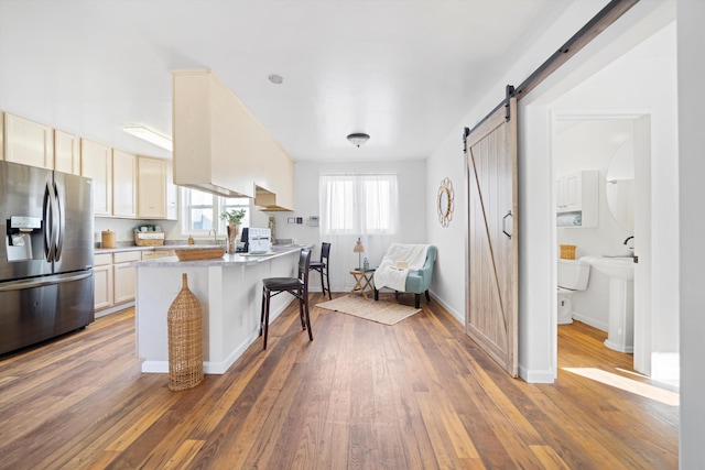 kitchen with stainless steel fridge, hardwood / wood-style flooring, a breakfast bar, light countertops, and a barn door