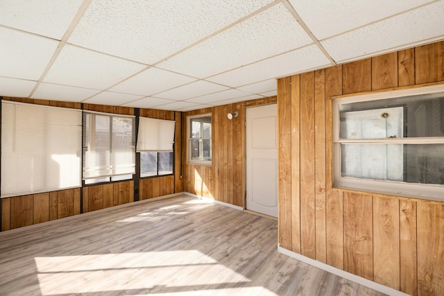 empty room with a drop ceiling, baseboards, wooden walls, and wood finished floors