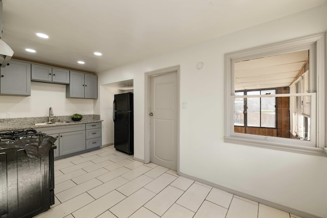 kitchen with light stone counters, recessed lighting, gray cabinets, freestanding refrigerator, and a sink