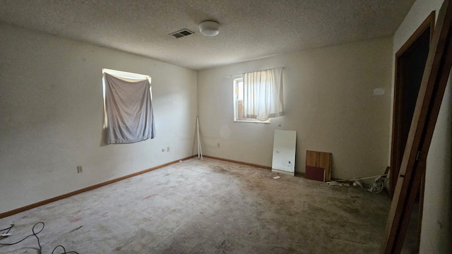 carpeted empty room featuring a textured ceiling, visible vents, and baseboards