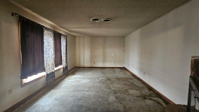 spare room with a healthy amount of sunlight, a textured ceiling, baseboards, and concrete flooring