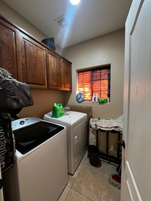 clothes washing area with washer and dryer, cabinets, and light tile patterned floors