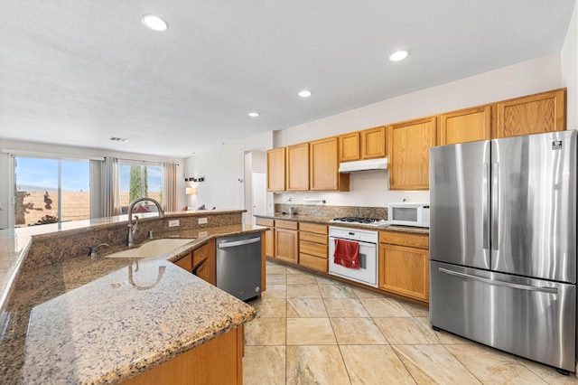 kitchen with light stone countertops, a sink, stainless steel appliances, recessed lighting, and under cabinet range hood