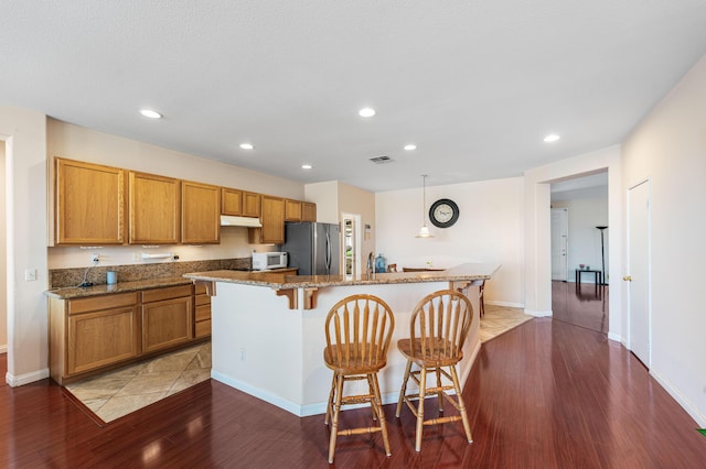 kitchen featuring a breakfast bar area, light wood-style flooring, freestanding refrigerator, white microwave, and a kitchen island