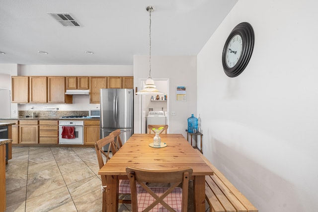 kitchen featuring visible vents, pendant lighting, washer / dryer, under cabinet range hood, and stainless steel appliances