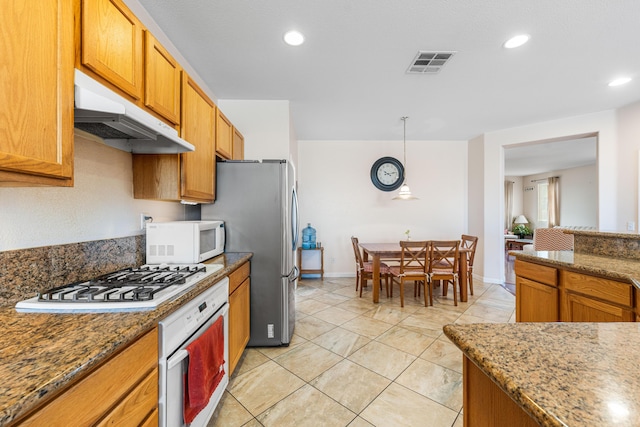 kitchen with visible vents, dark stone counters, under cabinet range hood, and white appliances