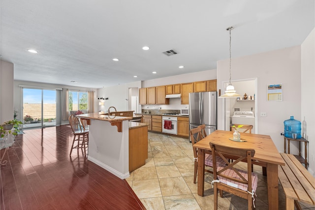 kitchen featuring visible vents, white appliances, an island with sink, a breakfast bar area, and under cabinet range hood