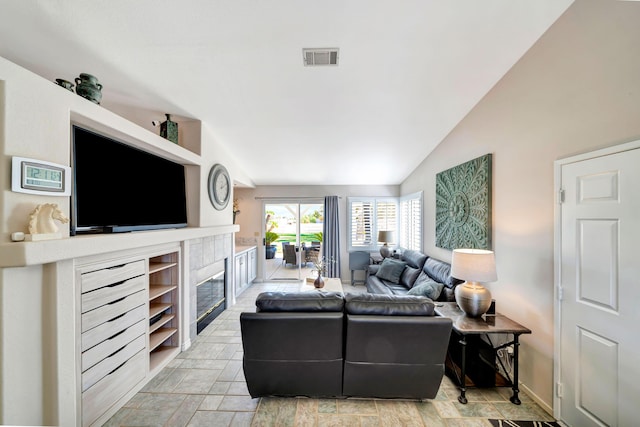 living room with built in shelves, a tile fireplace, and vaulted ceiling