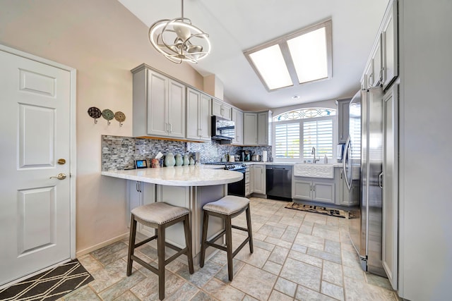 kitchen with a kitchen bar, kitchen peninsula, gray cabinetry, stainless steel appliances, and pendant lighting