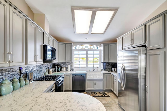 kitchen featuring sink, gray cabinets, appliances with stainless steel finishes, tasteful backsplash, and light stone counters