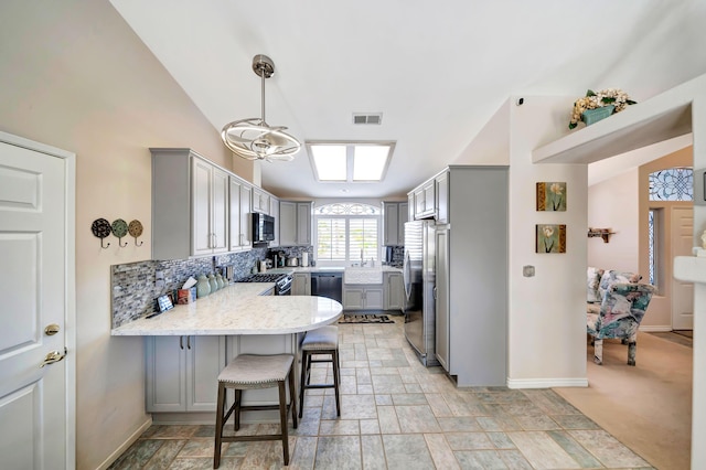 kitchen with kitchen peninsula, appliances with stainless steel finishes, decorative light fixtures, gray cabinets, and a breakfast bar area