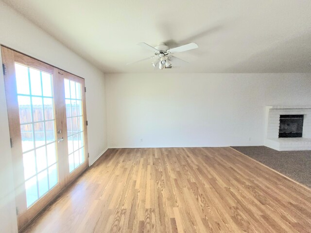 unfurnished living room featuring a fireplace, french doors, light hardwood / wood-style flooring, and ceiling fan