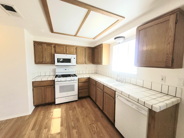 kitchen with white appliances, tile counters, dark wood-type flooring, and sink