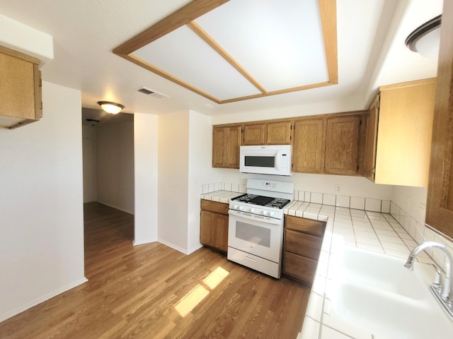 kitchen with light wood-type flooring, white appliances, tile countertops, and sink