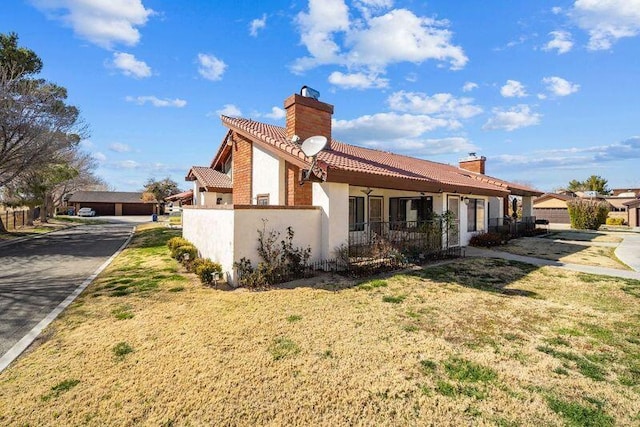 back of property featuring a tiled roof, a lawn, a chimney, and stucco siding