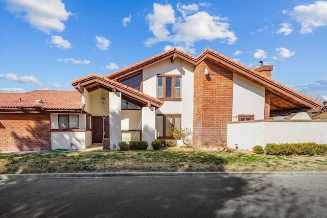 view of front of house featuring a tiled roof, a chimney, fence, and stucco siding