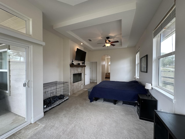 24500 Jacaranda Dr, Tehachapi, CA 93561 - carpeted bedroom with a tray ceiling, arched walkways, access to outside, a tiled fireplace, and ceiling fan