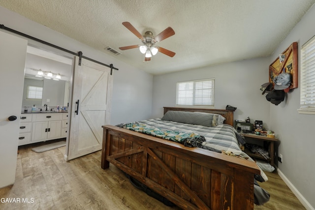 20412 El Porto Ct, Tehachapi, CA 93561 - bedroom featuring a barn door, light wood-type flooring, multiple windows, a textured ceiling, and ensuite bath
