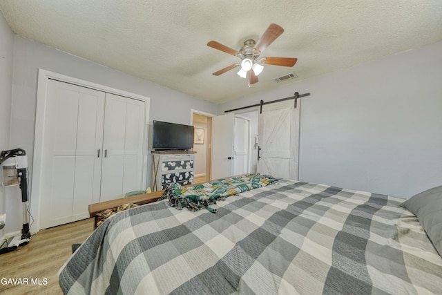 20412 El Porto Ct, Tehachapi, CA 93561 - bedroom with light wood-style flooring, a closet, a textured ceiling, a barn door, and a ceiling fan