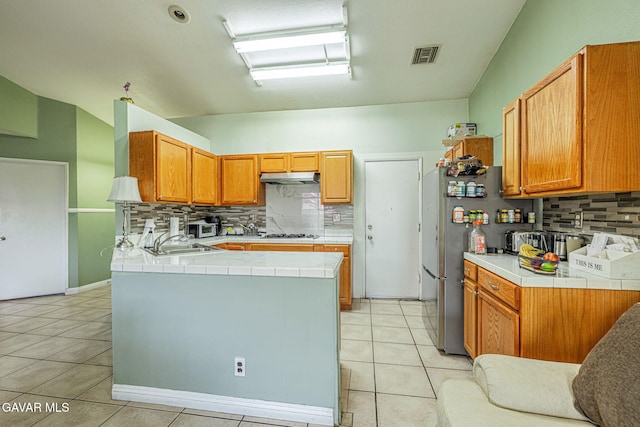 6019 Diamond St, Palmdale, CA 93552 - kitchen featuring under cabinet range hood, tasteful backsplash, tile countertops, light tile patterned floors, and a peninsula
