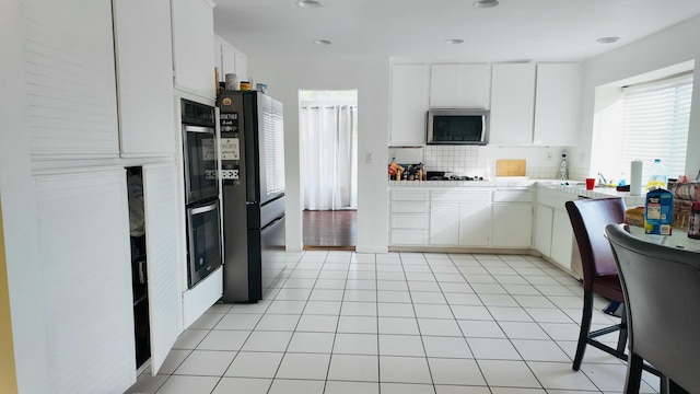 kitchen with white cabinets, backsplash, light tile patterned flooring, and black appliances