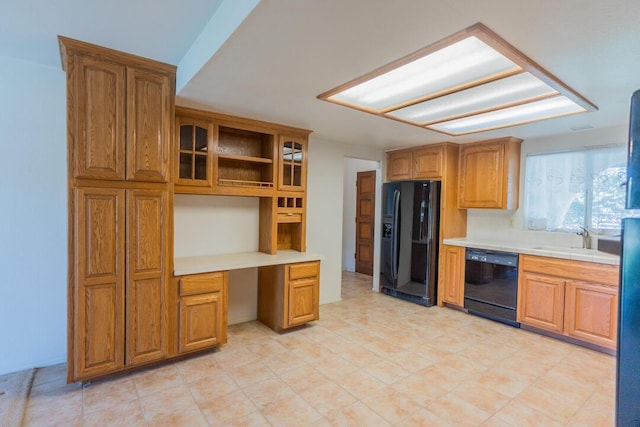 kitchen with brown cabinetry, built in desk, light countertops, black appliances, and glass insert cabinets