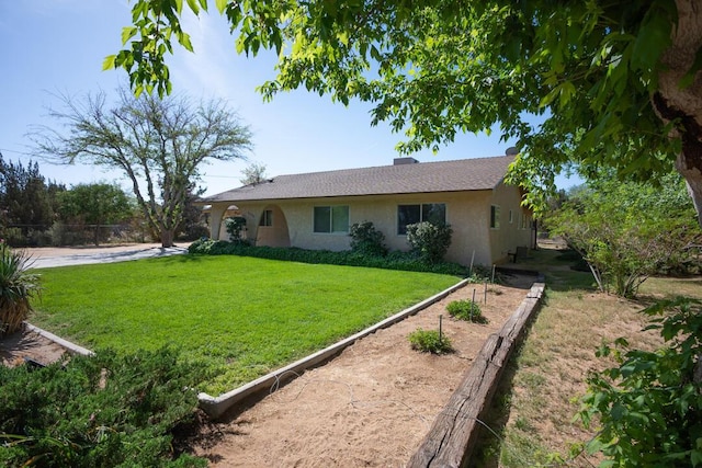 back of property with a lawn, fence, stucco siding, and a vegetable garden