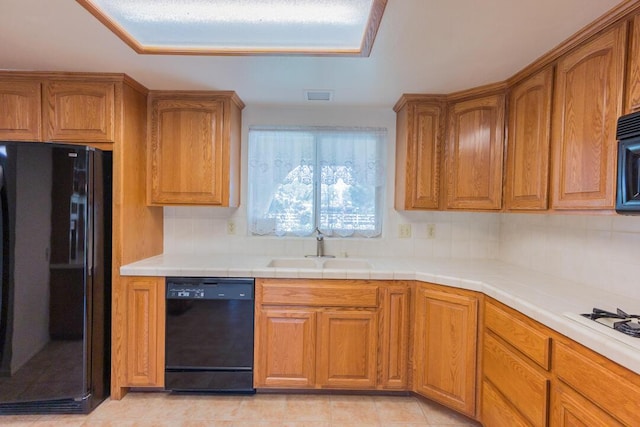 kitchen featuring brown cabinetry, a sink, backsplash, and black appliances
