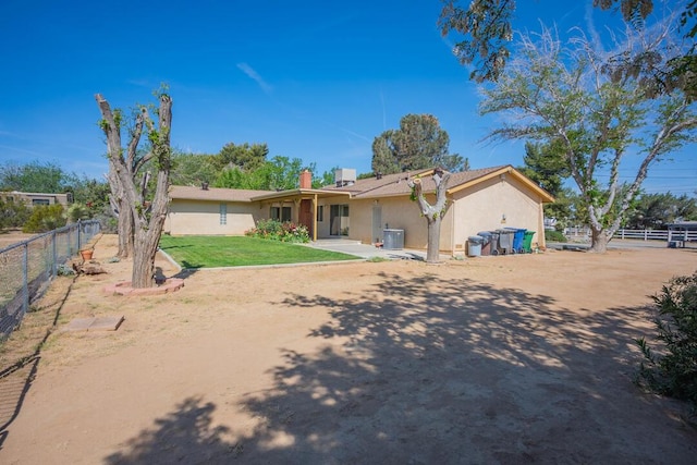 rear view of property featuring central air condition unit, a yard, fence, and stucco siding
