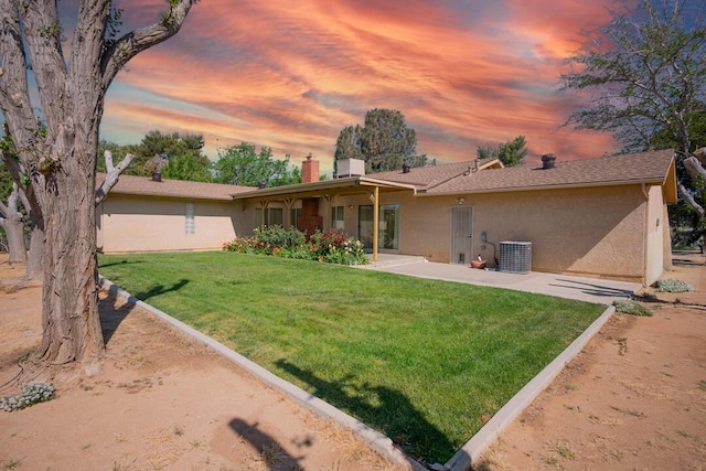 back of house at dusk with a lawn, a patio, a chimney, and stucco siding