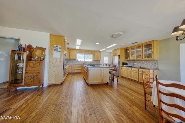 19426 Cavalier Ct, Tehachapi, CA 93561 - kitchen featuring appliances with stainless steel finishes, wood finished floors, decorative backsplash, glass insert cabinets, and a kitchen island