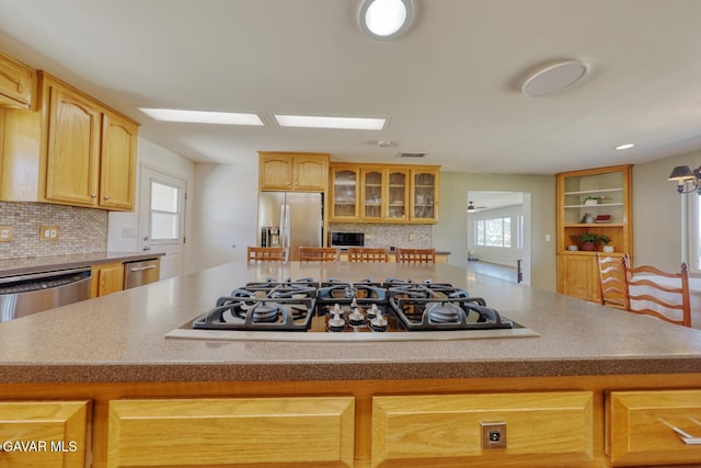 19426 Cavalier Ct, Tehachapi, CA 93561 - kitchen with stainless steel appliances, a center island, decorative backsplash, glass insert cabinets, and light brown cabinetry