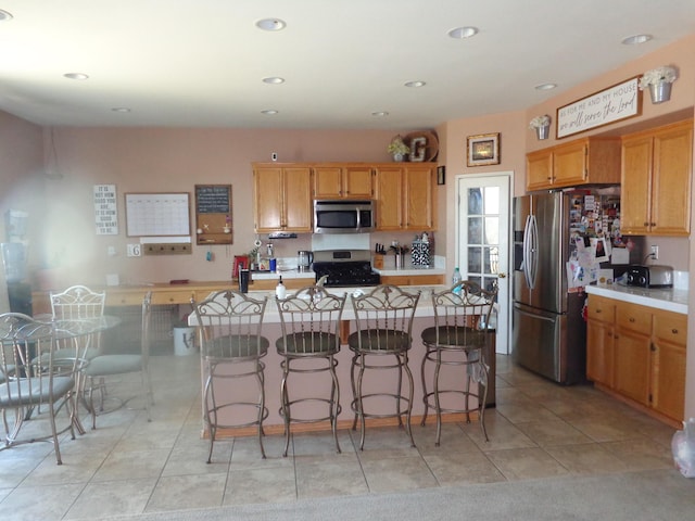 kitchen featuring appliances with stainless steel finishes, a center island, light tile patterned floors, and a kitchen breakfast bar